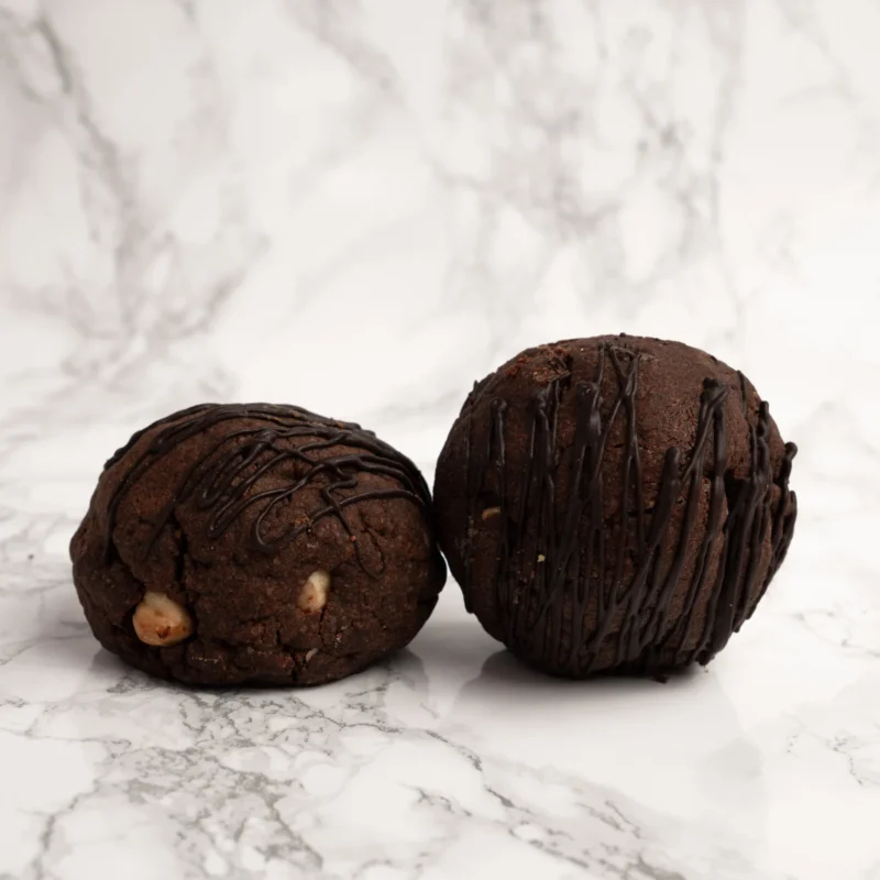 Två tjocka chokladcookies med hasselnötter och chokladdrizzle mot marmorbakgrund