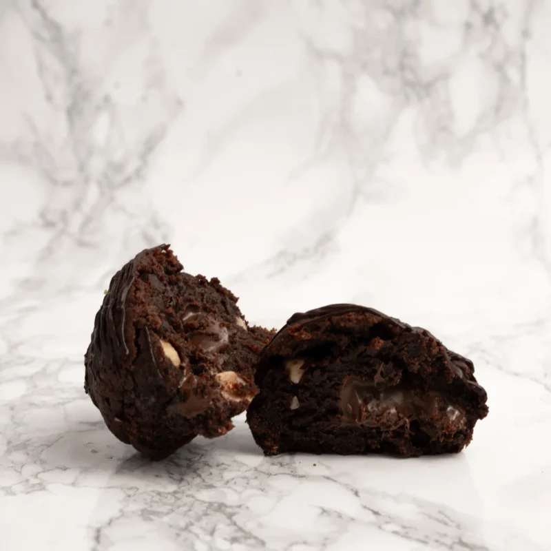 Tjock chokladcookie delad på mitten med synlig smält chokladfyllning och hela hasselnötter inuti