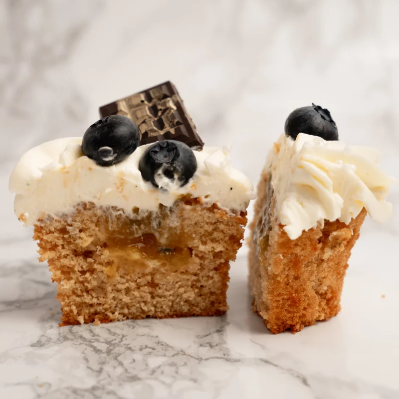 Genomskuren cupcake med krämig karamellfyllning, vitchokladfrosting, färska blåbär och chokladbit på marmorbord