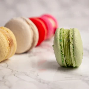 Grön macaron i fokus framför rad av färgglada macarons mot marmorbakgrund