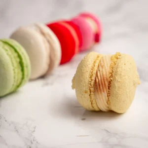Gul macaron med karamellfyllning i fokus framför rad av macarons mot marmorbakgrund