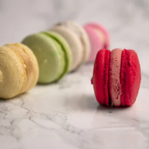 Röd macaron i fokus framför rad av färgglada macarons mot marmorbakgrund