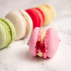 Rosa macaron med hallonfyllning i fokus framför rad av macarons mot marmorbakgrund