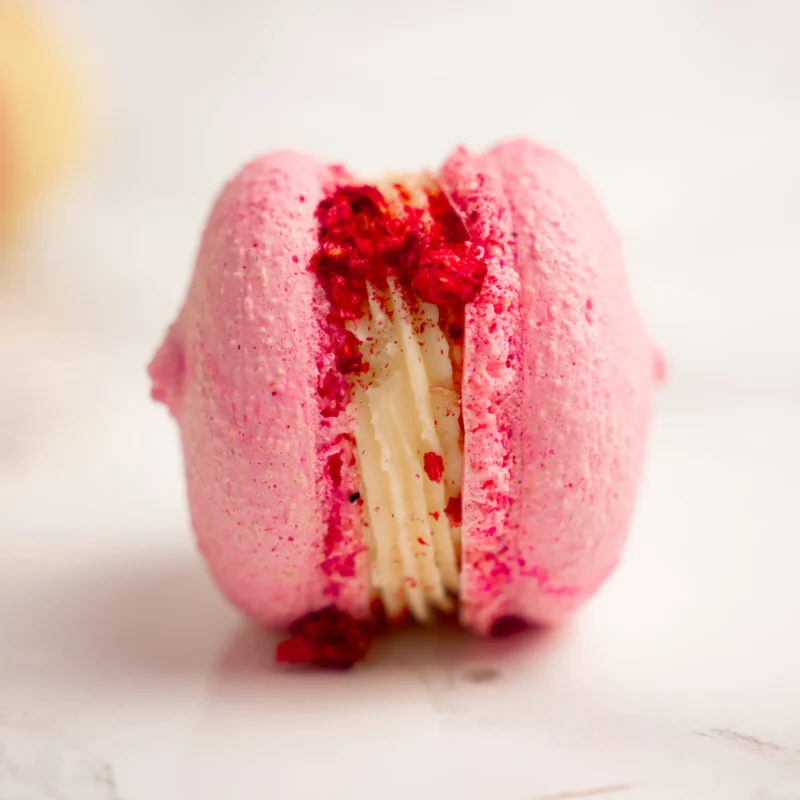 Extrem närbild på rosa macaron med hallonfyllning och krämigt lager synligt