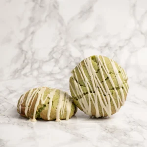 Två matchagröna cookies med vit chokladdrizzle mot marmorbakgrund