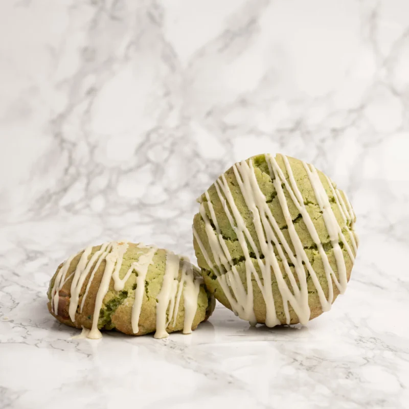 Två matchagröna cookies med vit chokladdrizzle mot marmorbakgrund