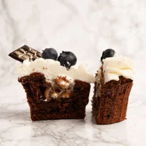 Mörk cupcake delad på mitten med synlig karamellfyllning, vispgrädde, blåbär och chokladbit på toppen