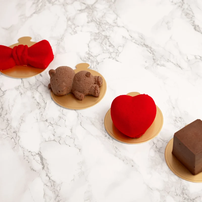 Fyra moussedesseter i olika former ovanifrån: röd rosett, chokladbjörn, rött hjärta och chokladkub