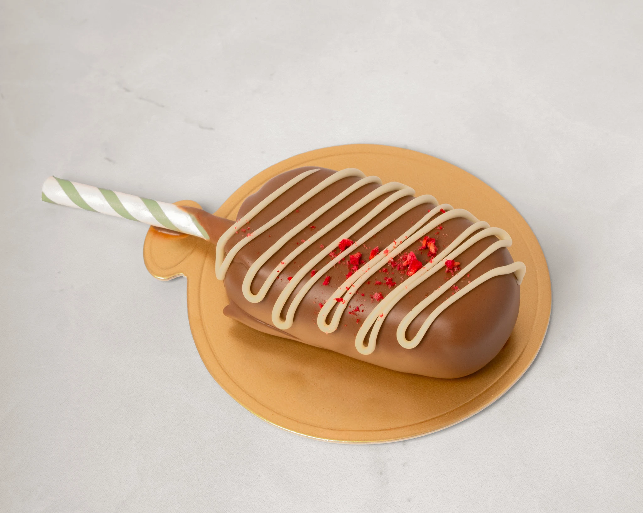 Närbild på popsicle cake täckt med mjölkchoklad, vitchokladränder och frystorkade jordgubbar på guldtallrik