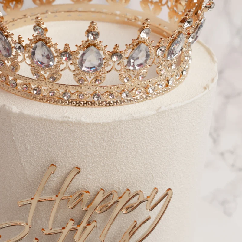 Närbild på Princess tårtas guldkrona med kristaller och Happy Birthday-topper i guld