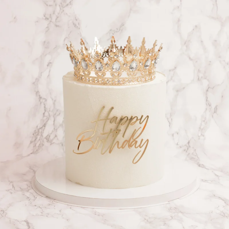 Princess tårta framifrån med guldkrona dekorerad med kristaller och Happy Birthday-text mot marmorbakgrund