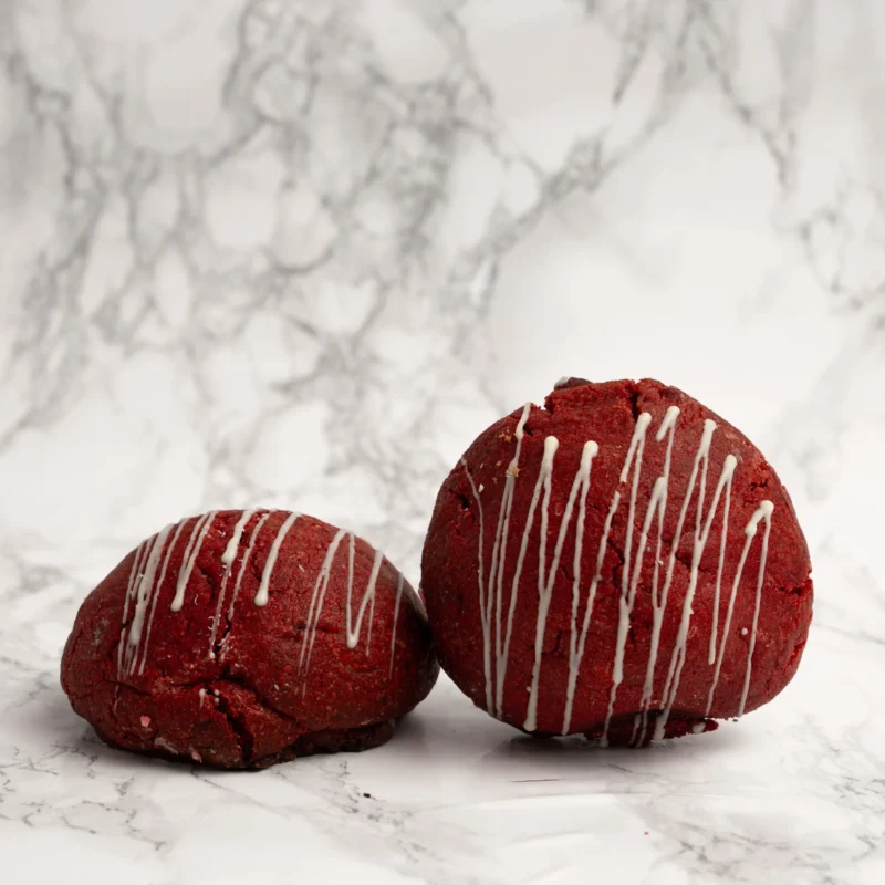 Två röda red velvet cookies med vit chokladdrizzle mot marmorbakgrund