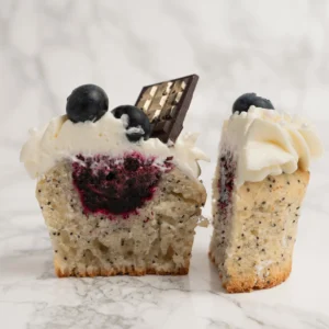 Vallmofrö-cupcake delad på mitten med synlig blåbärsfyllning, vispgrädde, blåbär och chokladbit på toppen