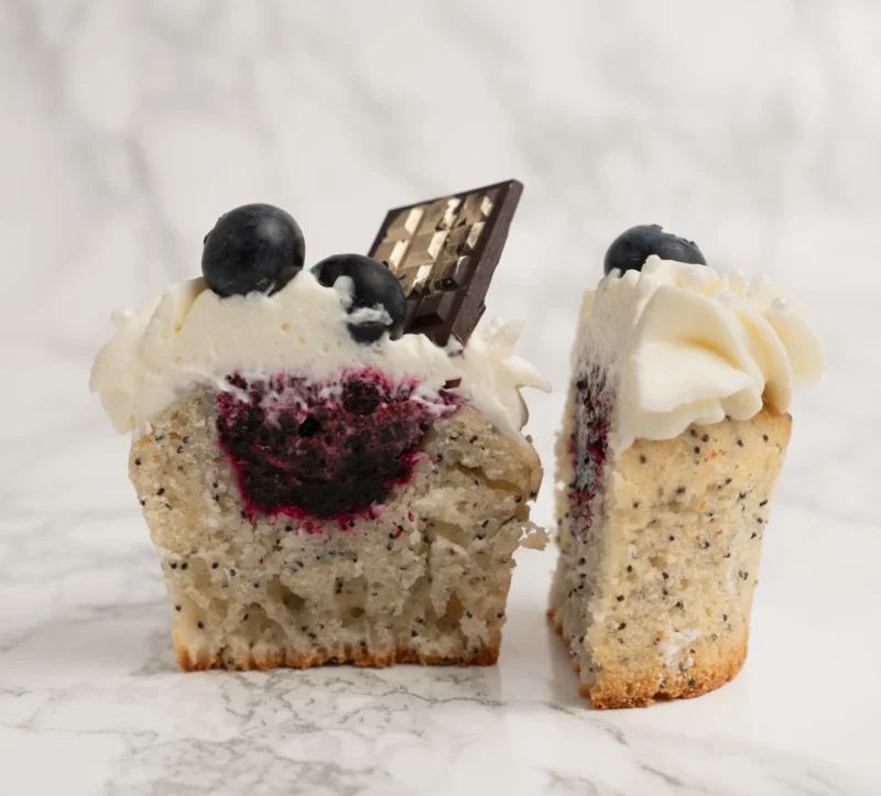 Vallmofrö-cupcake delad på mitten med synlig blåbärsfyllning, vispgrädde, blåbär och chokladbit på toppen