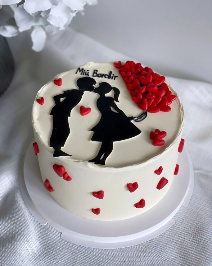 Tårta med romantiskt motiv av par och röda hjärtan på vit bakgrund.